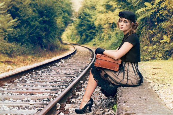 Ein Mädchen mit einem Hut und einem Koffer in der Hand sitzt in der Nähe der Eisenbahn