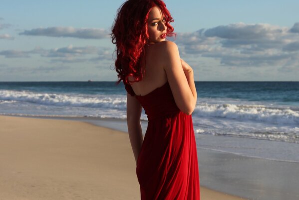Ein Mädchen mit roten Haaren und einem roten Kleid steht vor dem Hintergrund der Wellen