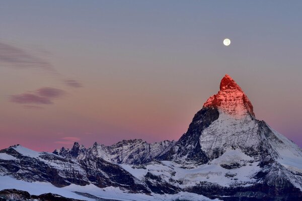 Der Gipfel der Alpen vor dem Hintergrund des zwielichtigen Himmels. Mond über dem Gipfel